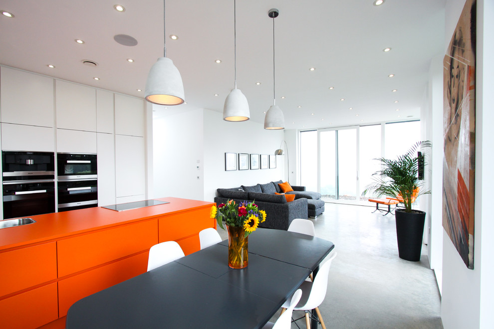 Contemporary open plan kitchen in Cheshire with orange cabinets, concrete flooring and an island.