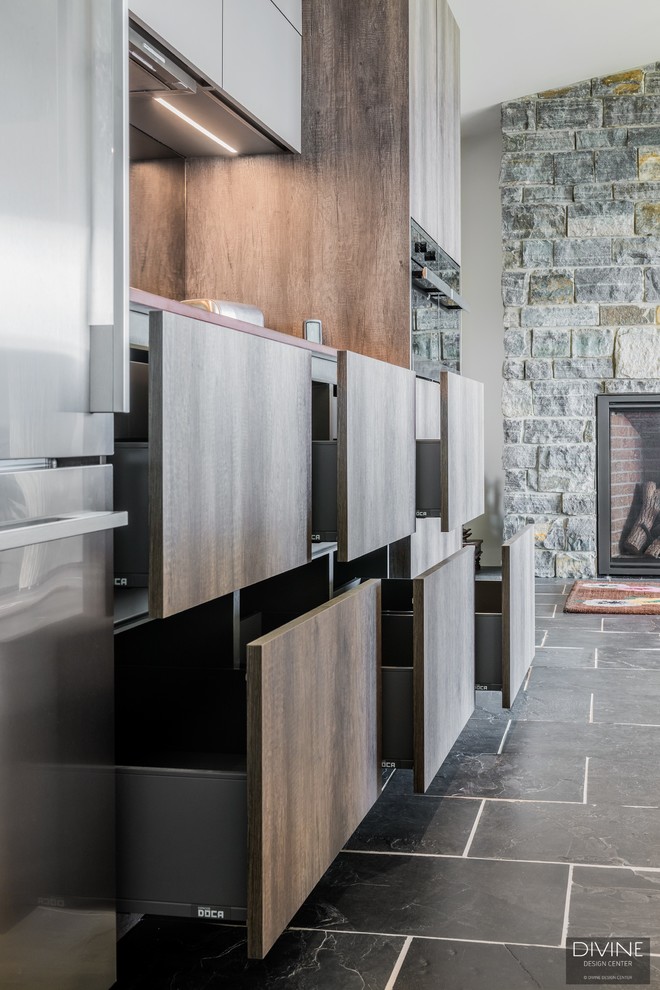 Photo of a large eclectic single-wall open plan kitchen in Boston with a farmhouse sink, flat-panel cabinets, dark wood cabinets, granite benchtops, metallic splashback, glass sheet splashback, stainless steel appliances, slate floors, with island, multi-coloured floor and brown benchtop.