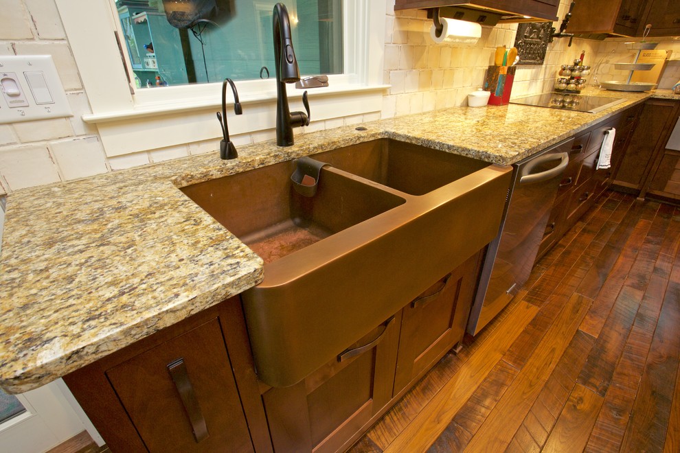 Large transitional l-shaped medium tone wood floor open concept kitchen photo with a farmhouse sink, shaker cabinets, medium tone wood cabinets, granite countertops, beige backsplash, stone tile backsplash, stainless steel appliances and an island