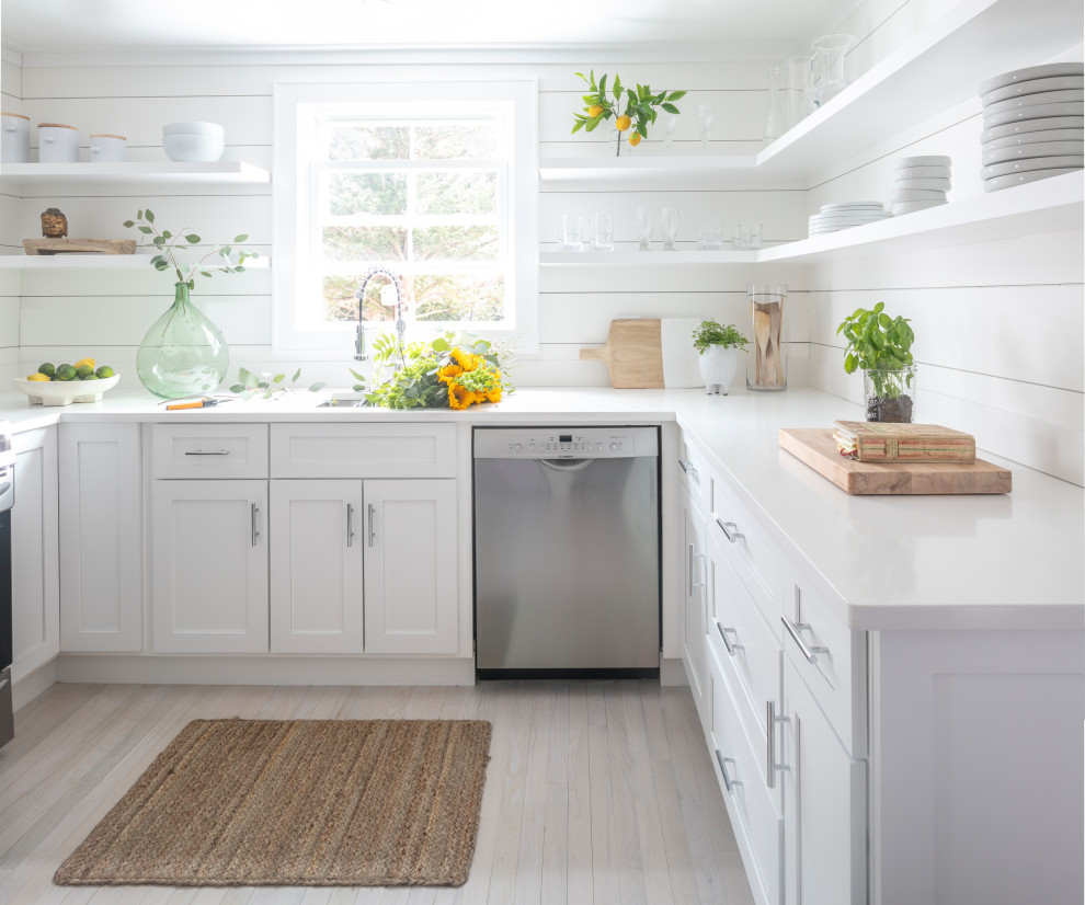 This is an example of a mid-sized beach style u-shaped separate kitchen in Other with a drop-in sink, shaker cabinets, white cabinets, quartz benchtops, white splashback, shiplap splashback, stainless steel appliances, light hardwood floors, no island, brown floor and white benchtop.