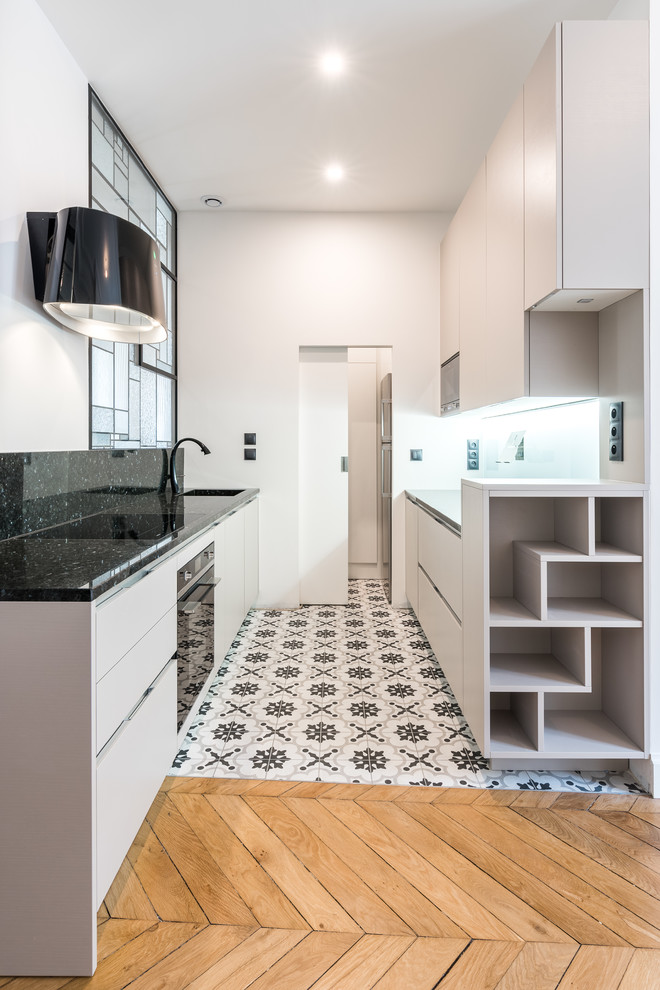 Inspiration for a small contemporary galley open plan kitchen in Lyon with an integrated sink, recessed-panel cabinets, beige cabinets, granite benchtops, black splashback, cement tile splashback, black appliances, cement tiles and no island.