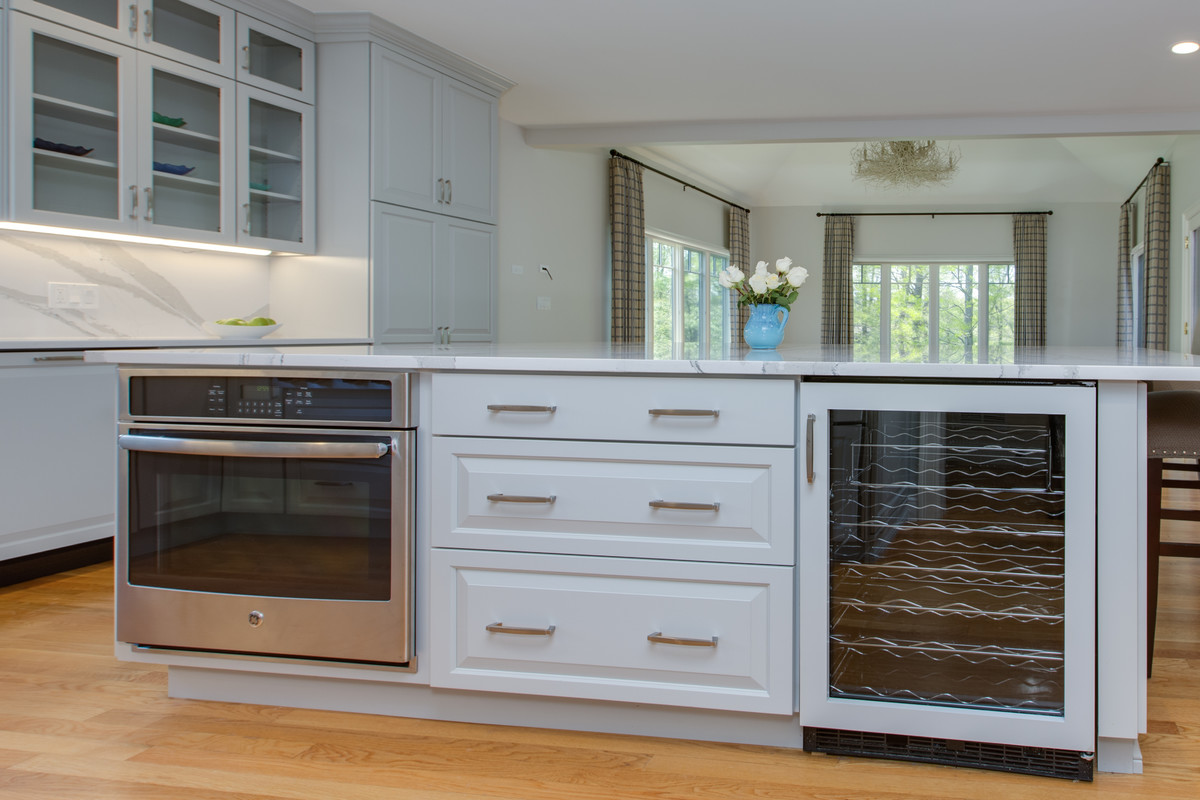Example of a large transitional l-shaped medium tone wood floor open concept kitchen design in Boston with an undermount sink, raised-panel cabinets, gray cabinets, quartz countertops, stone slab backsplash, paneled appliances and an island