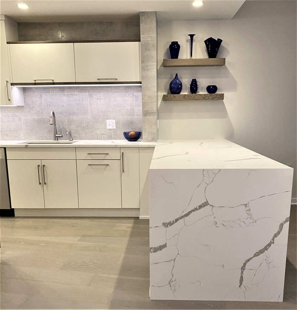 Mid-sized contemporary kitchen in New York with an undermount sink, flat-panel cabinets, white cabinets, quartz benchtops, grey splashback, porcelain splashback, stainless steel appliances and white benchtop.