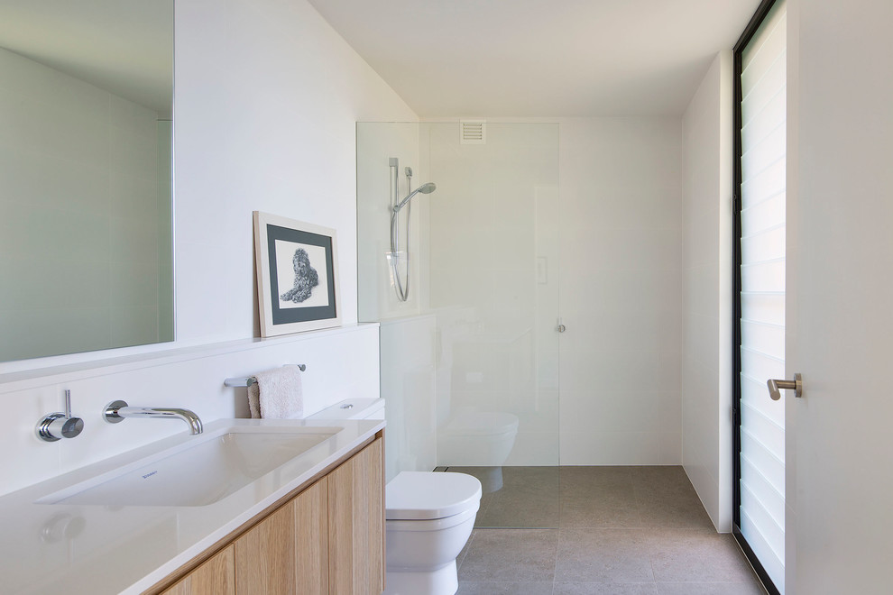 This is an example of a mid-sized contemporary 3/4 bathroom in Sydney with flat-panel cabinets, medium wood cabinets, an open shower, a one-piece toilet, white tile, ceramic tile, white walls, ceramic floors, an undermount sink, engineered quartz benchtops, beige floor and an open shower.