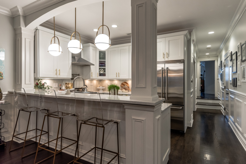 Mid-sized transitional u-shaped dark wood floor and brown floor eat-in kitchen photo in Chicago with a farmhouse sink, shaker cabinets, white cabinets, quartz countertops, gray backsplash, glass tile backsplash, stainless steel appliances, a peninsula and gray countertops