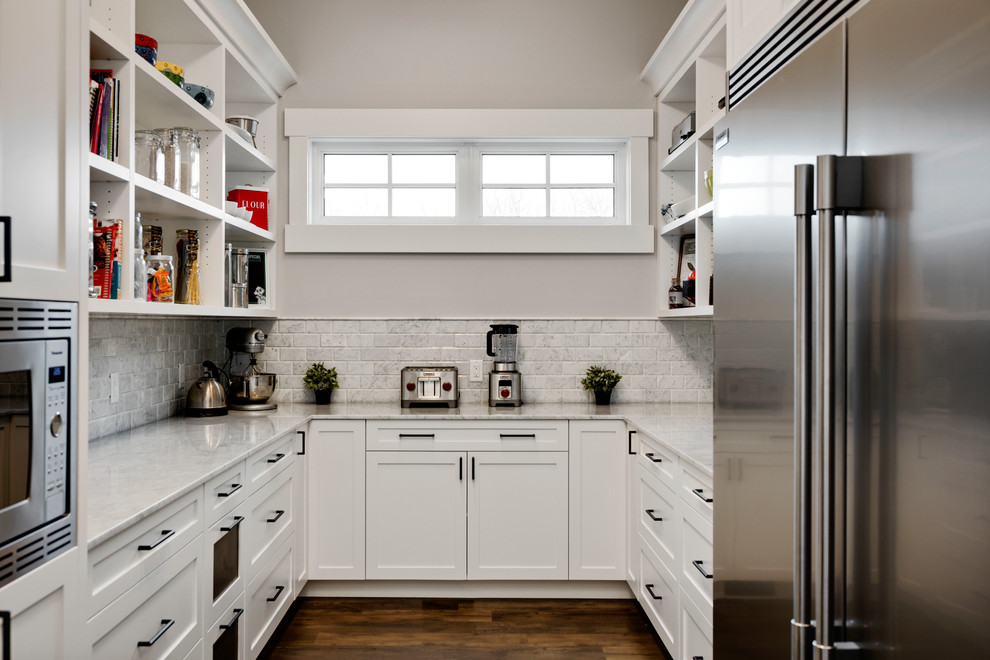 Huge transitional u-shaped dark wood floor and brown floor kitchen pantry photo in Calgary with shaker cabinets, white cabinets, marble countertops, gray backsplash, marble backsplash, stainless steel appliances and white countertops