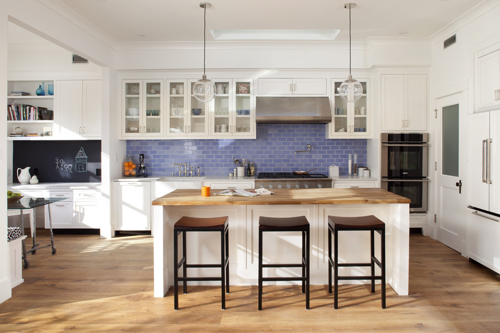 Photo of a contemporary kitchen in San Francisco with glass-front cabinets, panelled appliances, a farmhouse sink, wood benchtops, white cabinets, blue splashback and subway tile splashback.