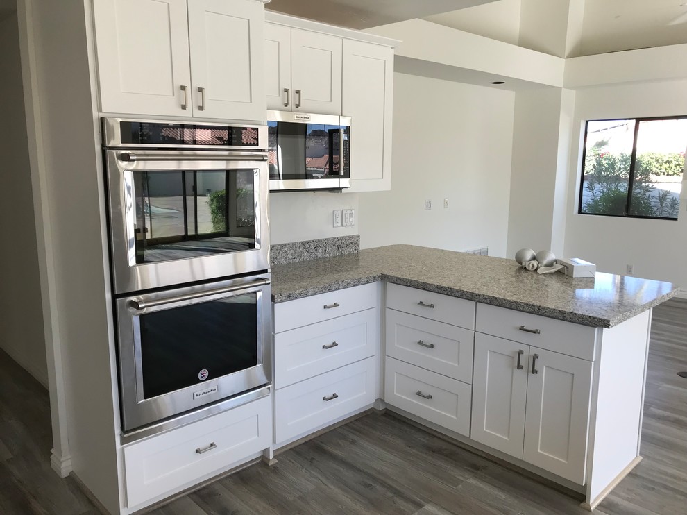 Inspiration for a transitional u-shaped laminate floor and gray floor open concept kitchen remodel with shaker cabinets, white cabinets, granite countertops, a peninsula, an undermount sink, gray backsplash, subway tile backsplash, stainless steel appliances and gray countertops
