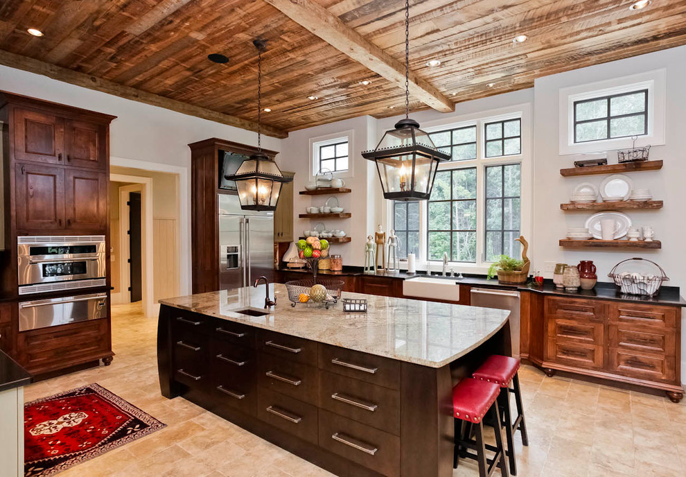 Large mountain style l-shaped travertine floor kitchen pantry photo with a farmhouse sink, recessed-panel cabinets, beige cabinets, granite countertops, beige backsplash, stone tile backsplash, stainless steel appliances and an island