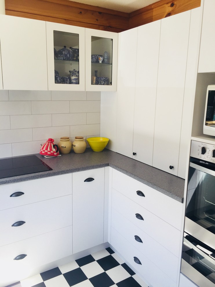 Mid-sized contemporary u-shaped separate kitchen in Christchurch with a single-bowl sink, flat-panel cabinets, white cabinets, laminate benchtops, white splashback, subway tile splashback, stainless steel appliances, vinyl floors, no island and black floor.