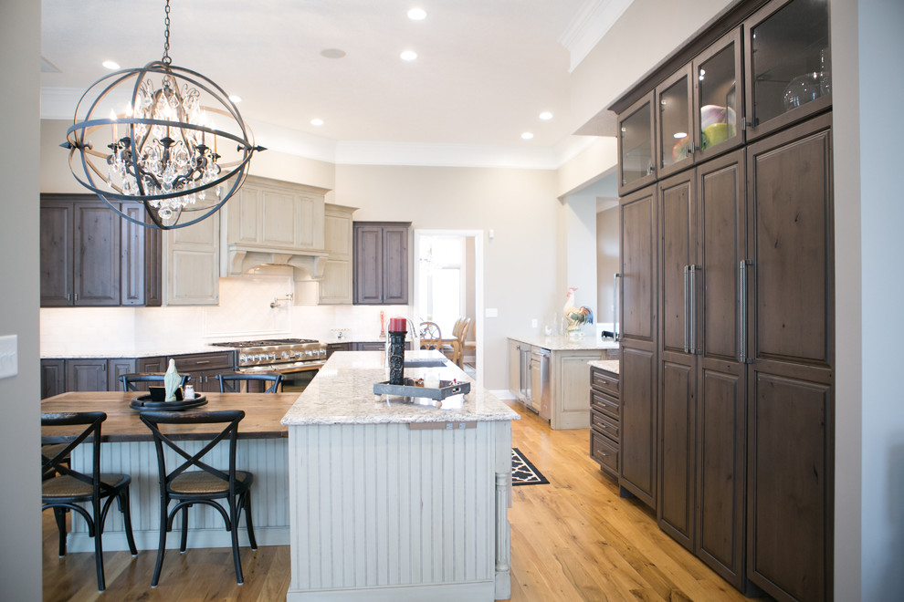 Inspiration for a large transitional u-shaped medium tone wood floor and brown floor kitchen remodel in Indianapolis with a farmhouse sink, raised-panel cabinets, dark wood cabinets, granite countertops, white backsplash, subway tile backsplash, paneled appliances, an island and multicolored countertops