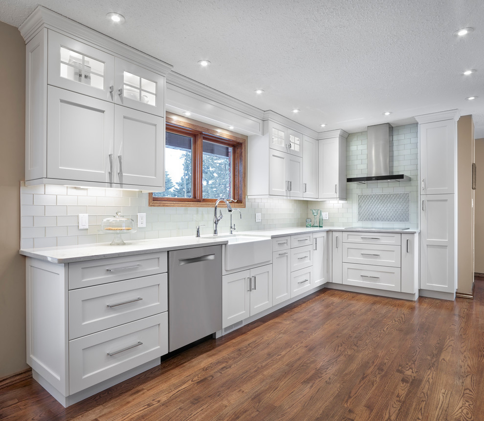 Inspiration for a mid-sized transitional l-shaped medium tone wood floor and brown floor eat-in kitchen remodel in Edmonton with a farmhouse sink, recessed-panel cabinets, white cabinets, quartz countertops, gray backsplash, glass tile backsplash, stainless steel appliances and no island