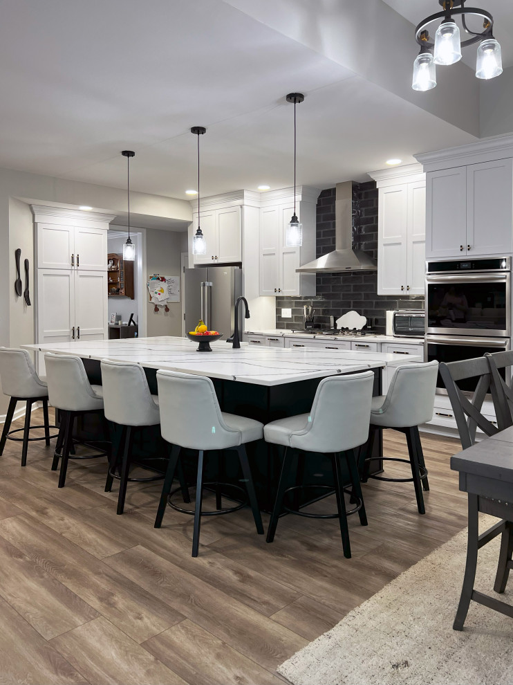 Large transitional single-wall vinyl floor and beige floor eat-in kitchen photo with a farmhouse sink, shaker cabinets, white cabinets, quartz countertops, black backsplash, subway tile backsplash, stainless steel appliances, an island and white countertops