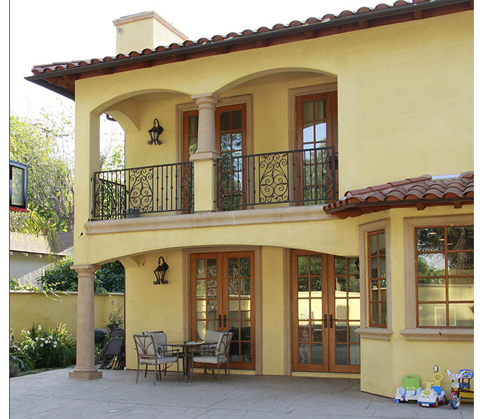 This is an example of a large traditional two-storey concrete yellow house exterior in Los Angeles with a gambrel roof and a shingle roof.