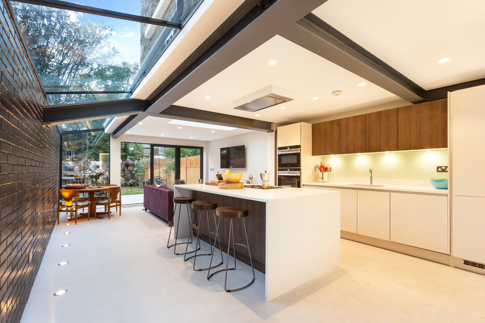 Inspiration for a contemporary open plan kitchen in London with with island, white floor, an undermount sink, flat-panel cabinets, white cabinets, white splashback, panelled appliances and white benchtop.