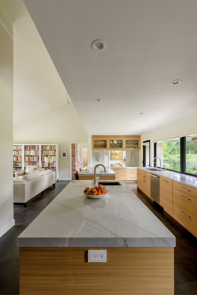 Inredning av ett modernt stort grå grått kök, med en undermonterad diskho, släta luckor, skåp i ljust trä, bänkskiva i kvartsit, grått stänkskydd, stänkskydd i porslinskakel, rostfria vitvaror, betonggolv, flera köksöar och grått golv