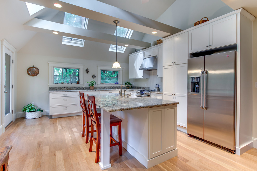 This is an example of a large traditional l-shaped eat-in kitchen in Boston with a farmhouse sink, shaker cabinets, white cabinets, granite benchtops, white splashback, stainless steel appliances, light hardwood floors, with island and subway tile splashback.