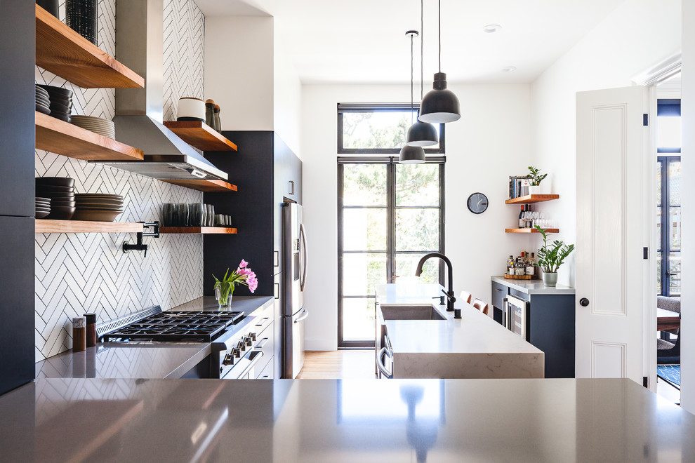 Photo of a mid-sized contemporary l-shaped kitchen pantry in San Francisco with a farmhouse sink, flat-panel cabinets, blue cabinets, quartz benchtops, white splashback, ceramic splashback, black appliances, medium hardwood floors, with island and grey benchtop.