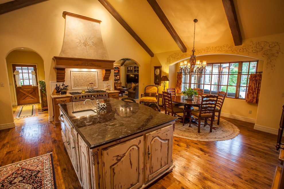 Photo of a large traditional u-shaped eat-in kitchen in Oklahoma City with an undermount sink, raised-panel cabinets, distressed cabinets, granite benchtops, white splashback, porcelain splashback, stainless steel appliances, dark hardwood floors and with island.