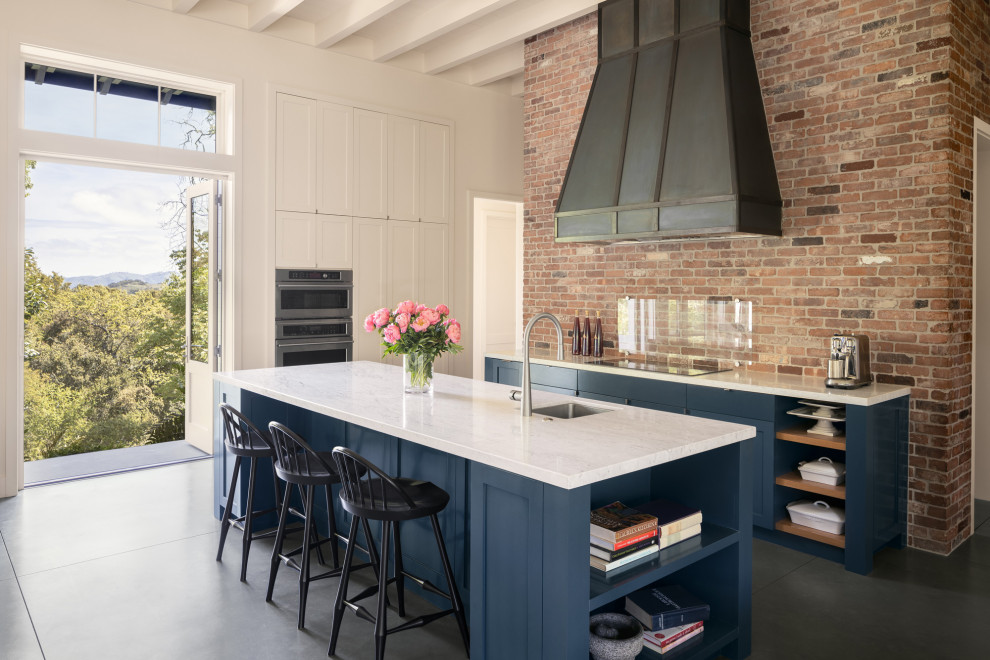 Photo of a large traditional single-wall open plan kitchen in San Francisco with a submerged sink, shaker cabinets, blue cabinets, marble worktops, multi-coloured splashback, brick splashback, stainless steel appliances, concrete flooring, an island, grey floors, white worktops and exposed beams.