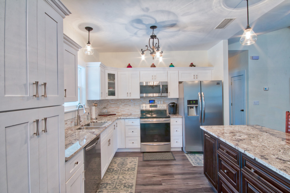 Example of a mid-sized l-shaped eat-in kitchen design with an undermount sink, shaker cabinets, yellow cabinets, granite countertops, glass tile backsplash, stainless steel appliances, an island and white countertops
