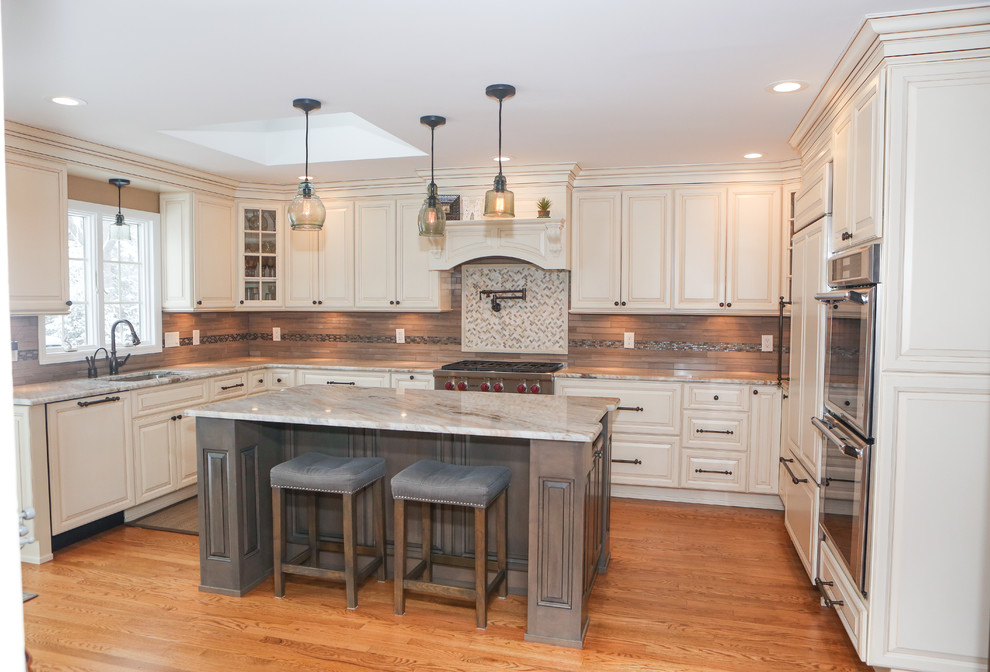 Eat-in kitchen - large transitional u-shaped light wood floor eat-in kitchen idea in Newark with an undermount sink, raised-panel cabinets, distressed cabinets, granite countertops, brown backsplash, mosaic tile backsplash, stainless steel appliances and an island