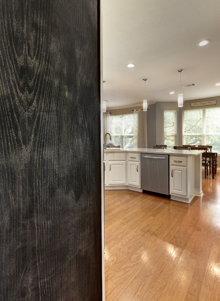 Mid-sized transitional u-shaped light wood floor eat-in kitchen photo in Austin with an undermount sink, white cabinets, quartz countertops, white backsplash, stone slab backsplash, stainless steel appliances, a peninsula and raised-panel cabinets