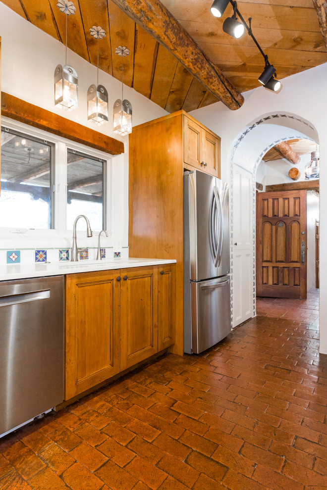 Inspiration for a mid-sized galley eat-in kitchen in Albuquerque with an undermount sink, shaker cabinets, medium wood cabinets, quartz benchtops, multi-coloured splashback, porcelain splashback, stainless steel appliances, brick floors, a peninsula, red floor and beige benchtop.