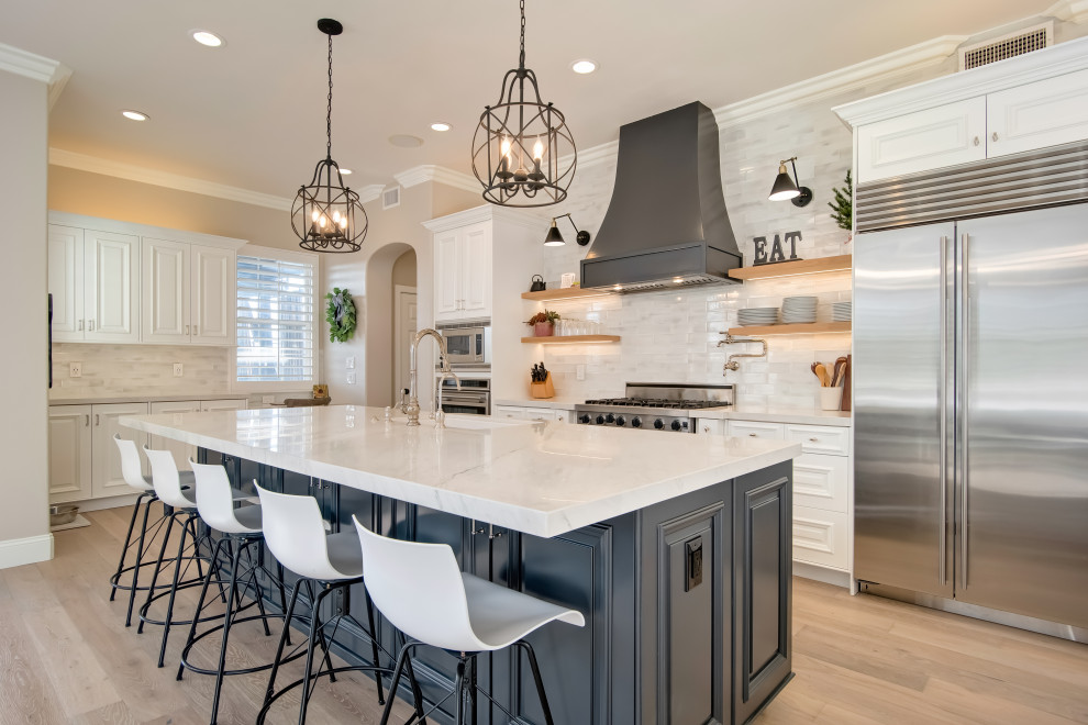 Traditional l-shaped kitchen in Orange County with an undermount sink, raised-panel cabinets, white cabinets, grey splashback, subway tile splashback, stainless steel appliances, medium hardwood floors, with island, brown floor and multi-coloured benchtop.