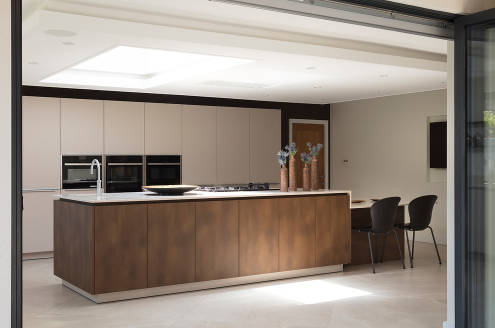 This is an example of a large contemporary l-shaped eat-in kitchen in London with an integrated sink, flat-panel cabinets, beige cabinets, quartzite benchtops, beige splashback, stone slab splashback, black appliances, porcelain floors, with island, beige floor and beige benchtop.