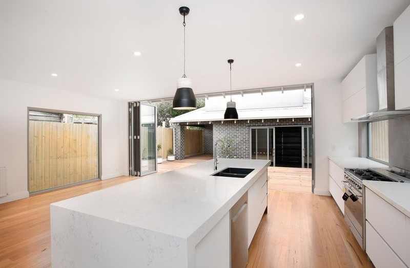This is an example of a large contemporary galley eat-in kitchen in Melbourne with a drop-in sink, flat-panel cabinets, white cabinets, quartz benchtops, grey splashback, window splashback, stainless steel appliances, light hardwood floors, with island, brown floor and white benchtop.