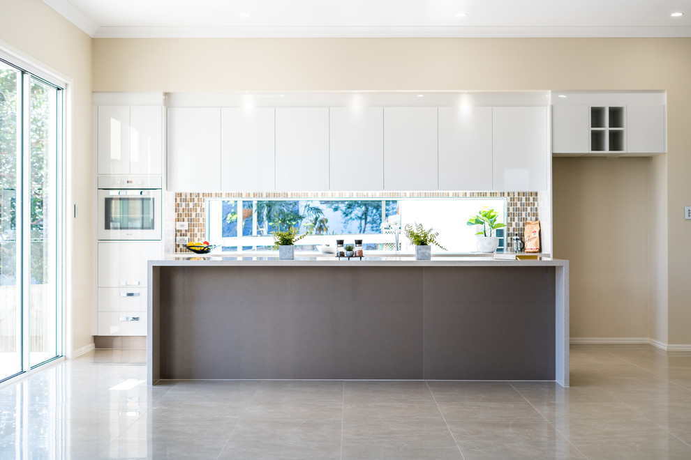 Design ideas for a mid-sized modern single-wall separate kitchen in Brisbane with a drop-in sink, raised-panel cabinets, white cabinets, limestone benchtops, brown splashback, brick splashback, coloured appliances, cement tiles, with island and grey floor.