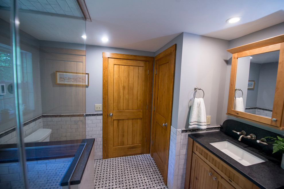 This is an example of an arts and crafts bathroom in Boston with shaker cabinets, light wood cabinets, a corner shower, white tile, grey walls, marble floors, an undermount sink and granite benchtops.