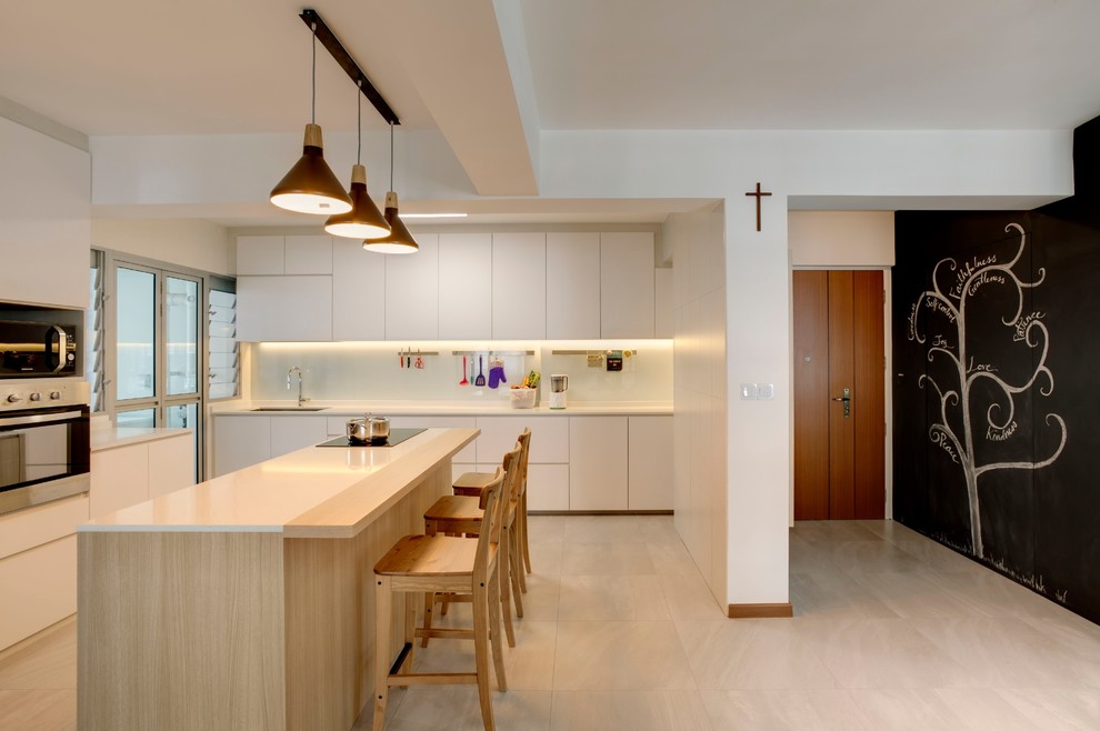 Photo of a contemporary l-shaped kitchen in Singapore with an undermount sink, flat-panel cabinets, white cabinets, white splashback, black appliances, with island, beige floor and white benchtop.