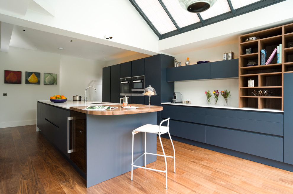 Photo of a large contemporary single-wall open plan kitchen in London with an undermount sink, flat-panel cabinets, blue cabinets, quartzite benchtops, black appliances, with island, brown floor, white splashback and medium hardwood floors.