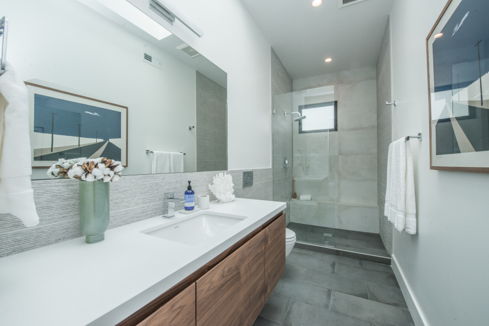 Photo of a small contemporary 3/4 bathroom in Los Angeles with flat-panel cabinets, medium wood cabinets, an open shower, a wall-mount toilet, gray tile, porcelain tile, white walls, porcelain floors, an undermount sink, engineered quartz benchtops, grey floor, a hinged shower door, white benchtops, a shower seat, a single vanity and a floating vanity.