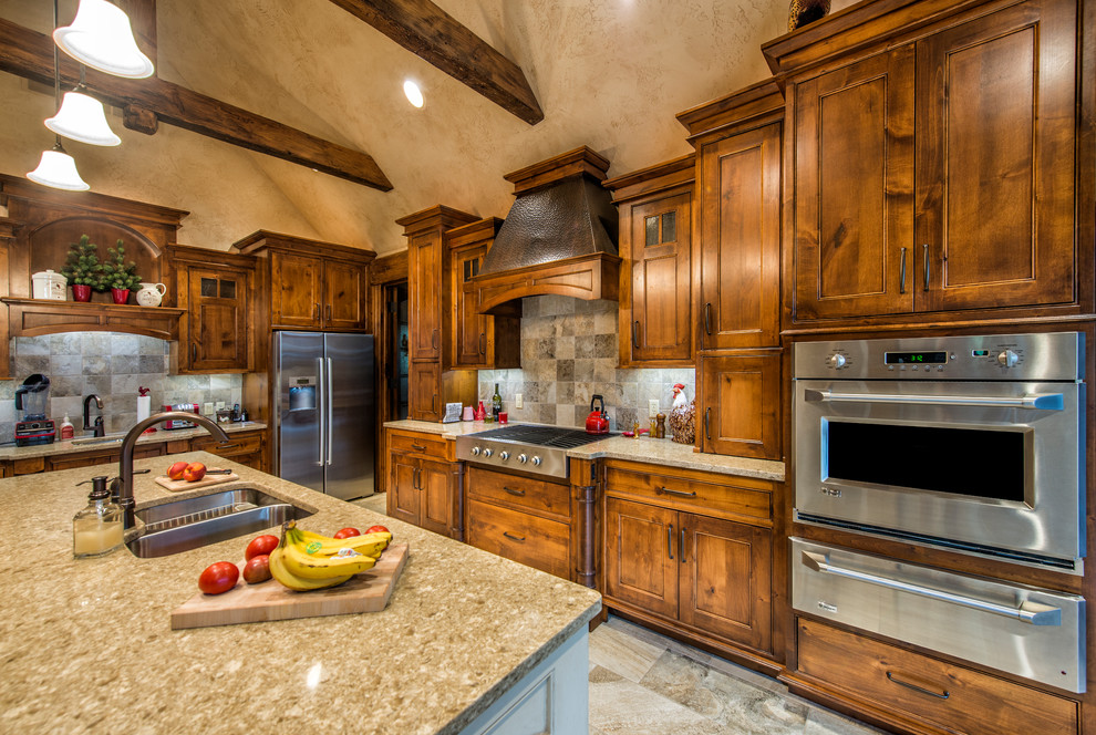 Kitchen - large rustic l-shaped porcelain tile kitchen idea with a double-bowl sink, beaded inset cabinets, medium tone wood cabinets, granite countertops, gray backsplash, ceramic backsplash, stainless steel appliances and an island