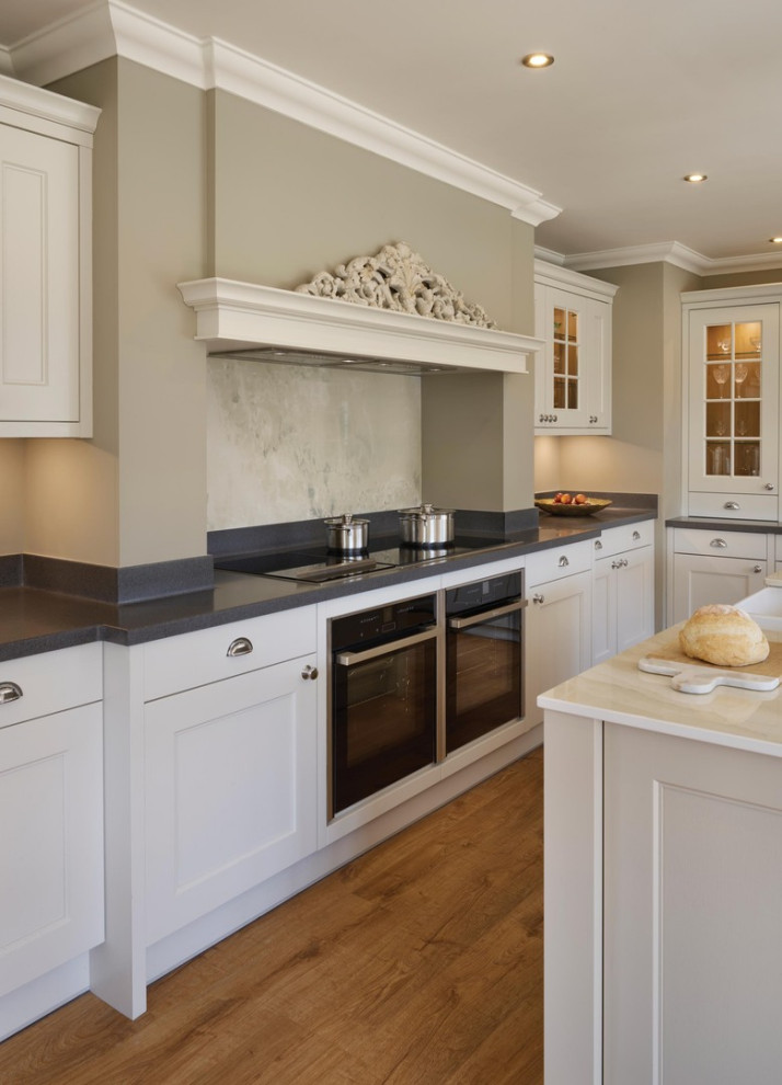 Design ideas for a large traditional l-shaped open plan kitchen in Essex with a farmhouse sink, shaker cabinets, beige cabinets, quartzite benchtops, grey splashback, granite splashback, panelled appliances, medium hardwood floors, with island, brown floor and white benchtop.