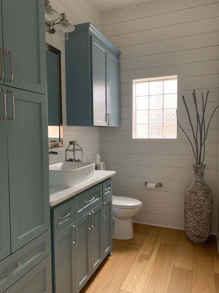 Klassisk inredning av ett mellanstort vit vitt badrum med dusch, med luckor med infälld panel, blå skåp, en toalettstol med hel cisternkåpa, vita väggar, ljust trägolv, ett fristående handfat, marmorbänkskiva och beiget golv