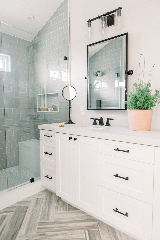 Photo of a mid-sized country master bathroom in San Diego with shaker cabinets, white cabinets, an alcove shower, a one-piece toilet, gray tile, glass tile, grey walls, porcelain floors, an undermount sink, engineered quartz benchtops, beige floor, a hinged shower door and white benchtops.