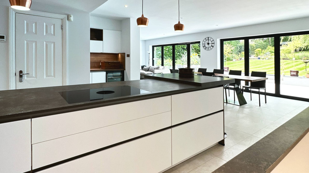 Idéer för stora minimalistiska grått kök, med en integrerad diskho, släta luckor, vita skåp, bänkskiva i kvartsit, svarta vitvaror, en köksö och grått golv