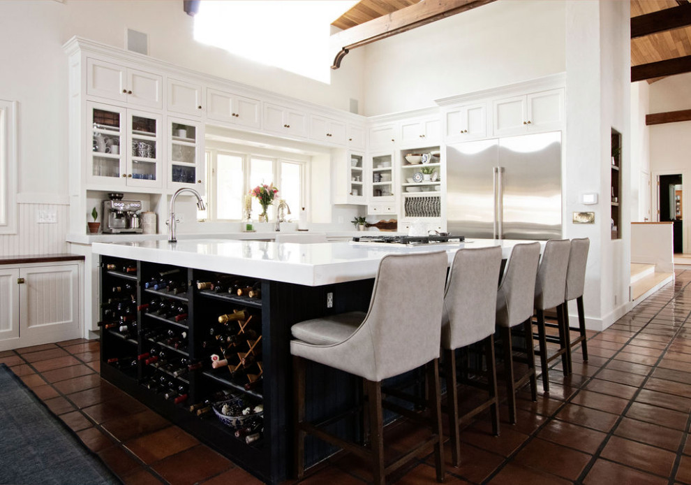 Photo of a large country eat-in kitchen in Kansas City with a farmhouse sink, glass-front cabinets, white cabinets, quartzite benchtops, white splashback, engineered quartz splashback, stainless steel appliances, terra-cotta floors, with island, multi-coloured floor, white benchtop and exposed beam.