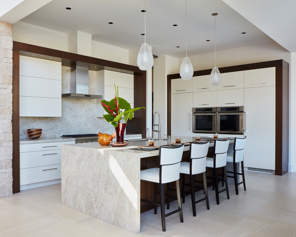 This is an example of a contemporary l-shaped kitchen in Miami with an undermount sink, flat-panel cabinets, white cabinets, beige splashback, stainless steel appliances, with island, beige floor and beige benchtop.