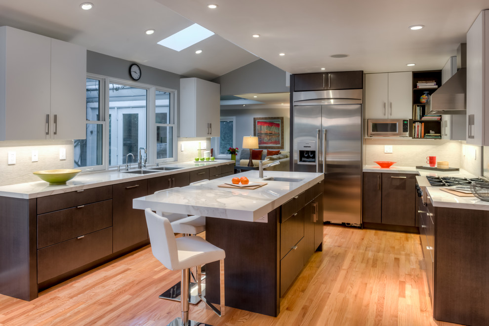 This is an example of a contemporary u-shaped kitchen in San Francisco with an undermount sink, flat-panel cabinets, dark wood cabinets, white splashback, stainless steel appliances, marble benchtops, light hardwood floors and with island.