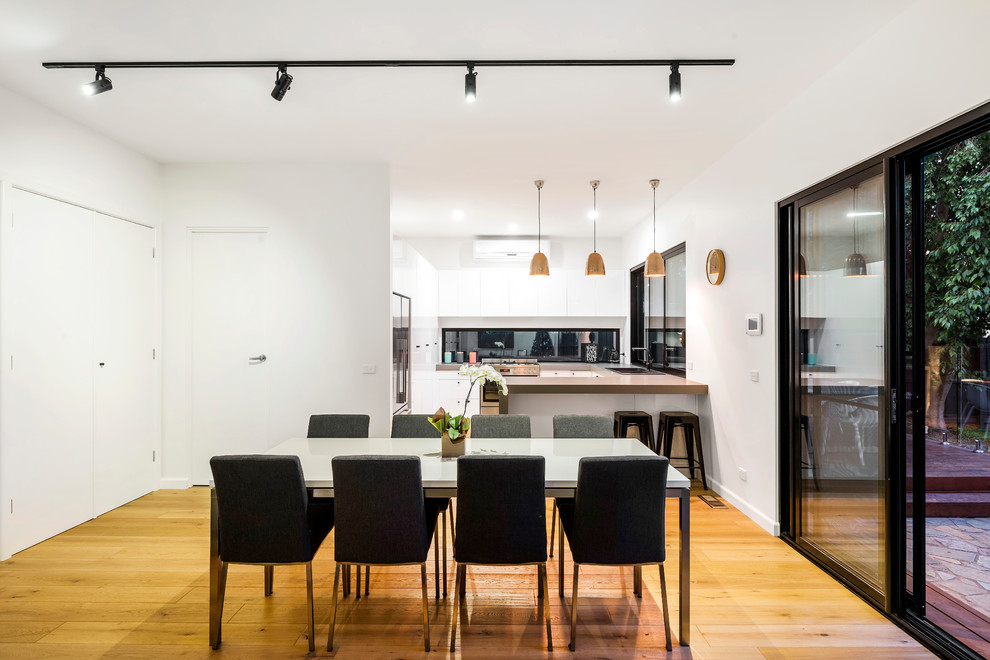 Photo of a mid-sized contemporary kitchen/dining combo in Melbourne with white walls, medium hardwood floors and no fireplace.