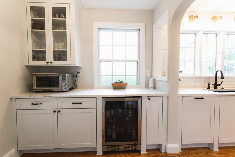 Inspiration for a large transitional l-shaped eat-in kitchen in Baltimore with an undermount sink, shaker cabinets, white cabinets, quartz benchtops, white splashback, marble splashback, stainless steel appliances, medium hardwood floors, with island, brown floor and white benchtop.