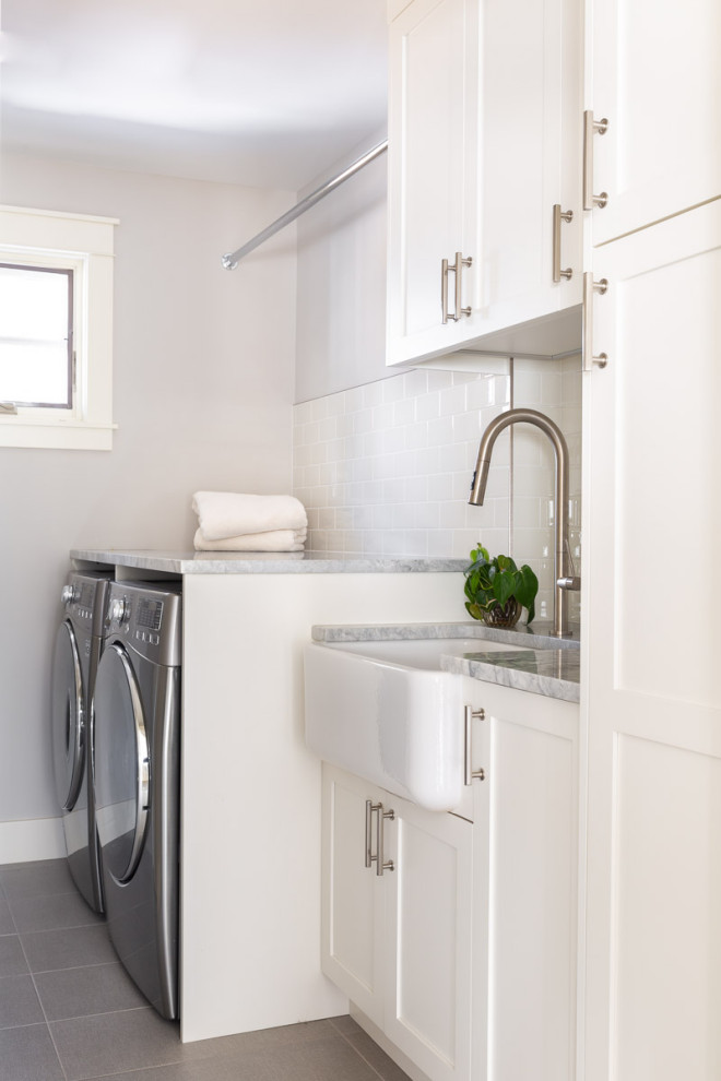Inspiration for a small modern single-wall dedicated laundry room in Calgary with a farmhouse sink, recessed-panel cabinets, white cabinets, quartz benchtops, white splashback, subway tile splashback, grey walls, porcelain floors, a side-by-side washer and dryer, grey floor and grey benchtop.