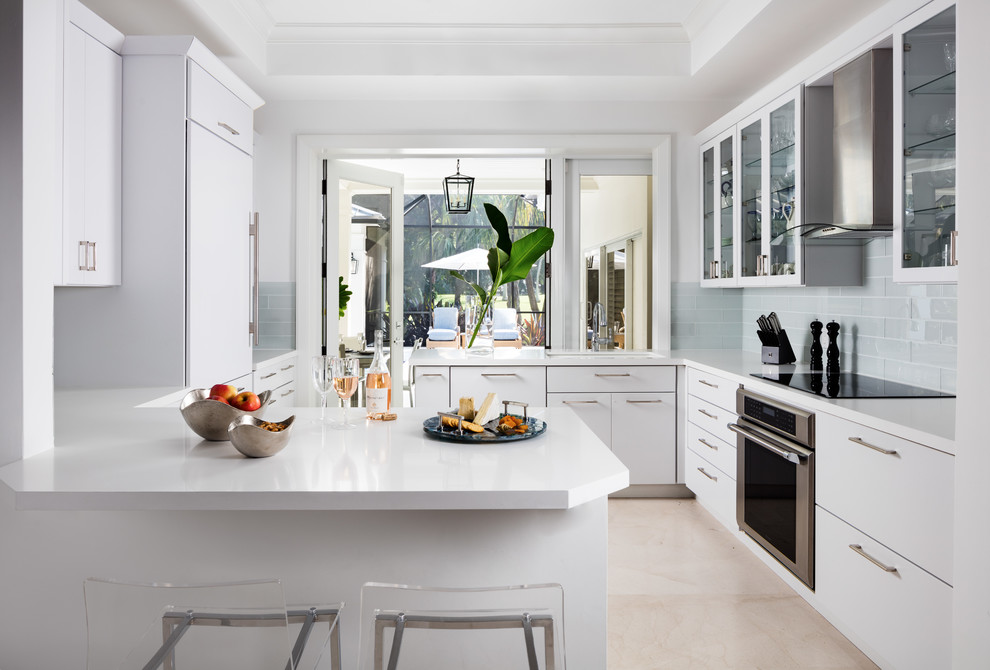 Inspiration for a mid-sized transitional u-shaped eat-in kitchen in Miami with flat-panel cabinets, white cabinets, solid surface benchtops, grey splashback, glass tile splashback, panelled appliances, marble floors, a peninsula and beige floor.