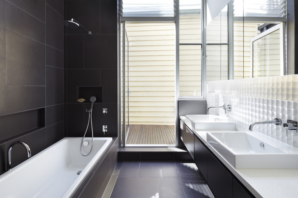 This is an example of a contemporary 3/4 bathroom in Melbourne with flat-panel cabinets, black cabinets, a drop-in tub, a shower/bathtub combo, black tile, white tile, a console sink, black floor and an open shower.