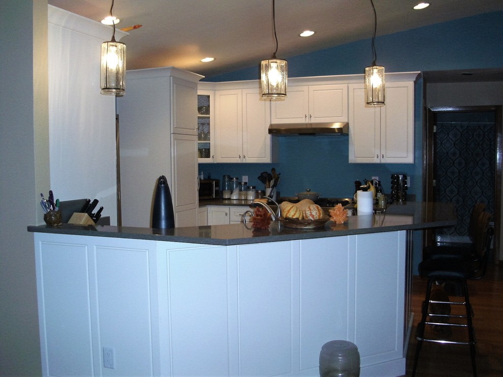 This is an example of a mid-sized transitional u-shaped eat-in kitchen in Milwaukee with a single-bowl sink, raised-panel cabinets, white cabinets, quartz benchtops, stainless steel appliances and vinyl floors.